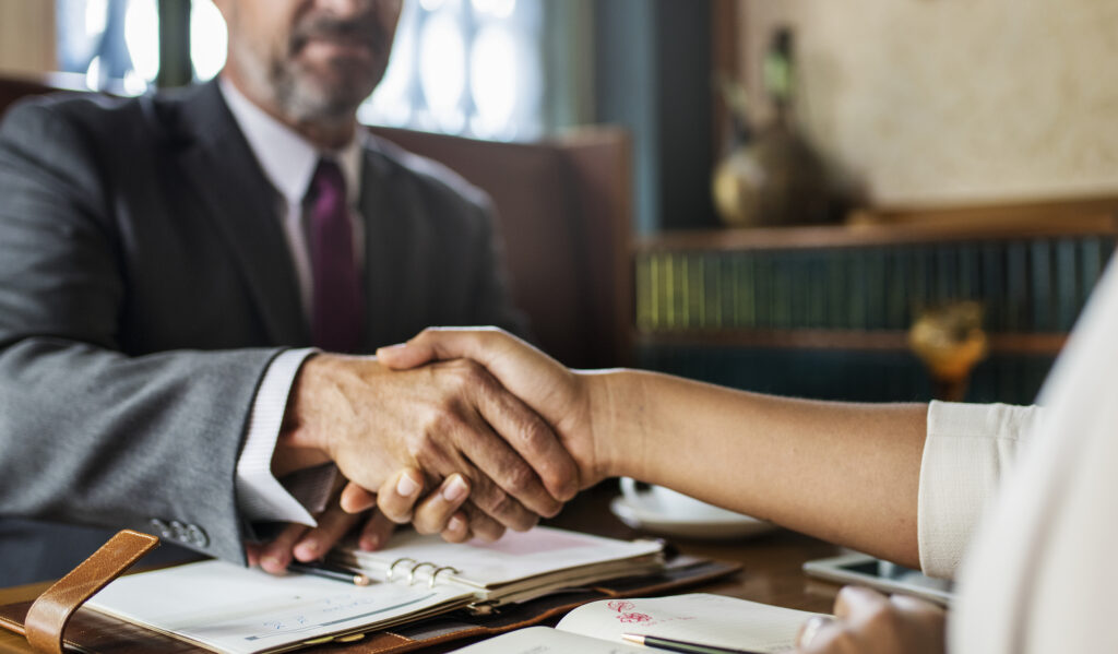 Aperto de mãos entre homem e mulher durante uma assinatura de contrato ou acordo de negócios, simbolizando parceria e confiança.